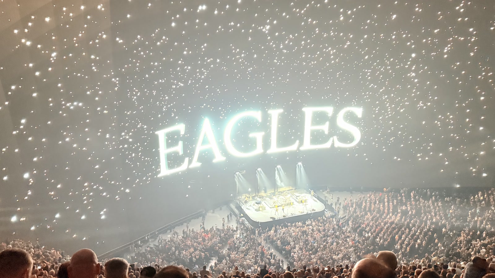 Concert finale: a glowing EAGLES sign over the starry dome sky, stage and audience below